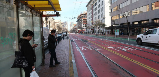 지나가는 차가 보이지 않는 마켓스트리트 버스 정류장에서 승객들이 버스를 기다리고 있다. 