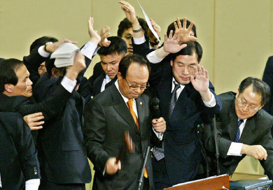 2004년 3월 12일 국회 본회의장에서 박관용 당시 국회의장이 노무현 대통령에 대한 탄핵안 가결을 선포한 뒤 방망이를 두드리고 있다. 열린우리당 의원들이 의석에서 박 의장을 향해 안건 뭉치와 각종 물건을 던지자 국회 직원들이 손으로 막고 있다. 동아DB