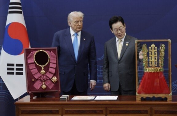 이재명 대통령이 경북 경주박물관에서 트럼프 대통령에게 무궁화 대훈장을 수여하고 천마총 금관 모형을 선물하고 있다. 무궁화 대훈장은 상훈법상 최고 등급 훈장으로, 미국 대통령이 받은 건 이번이 처음이다. 훈장 제작에는 금 190돈(약 712.5g), 은 110돈(약 412.5g)과 루비, 자수정, 칠보 등이 사용됐으며 제작비 중 금값만 약 1억3000만 원(10월 29일 기준)에 이르는 것으로 알려졌다. 이 대통령은 “대한민국 국민이 대통령님에게 각별한 감사의 마음을 담아서 드린다”고 말했고, 트럼프 대통령은 “무척 아름다운 선물이다. 소중히 간직하겠다”고 화답했다. 뉴시스