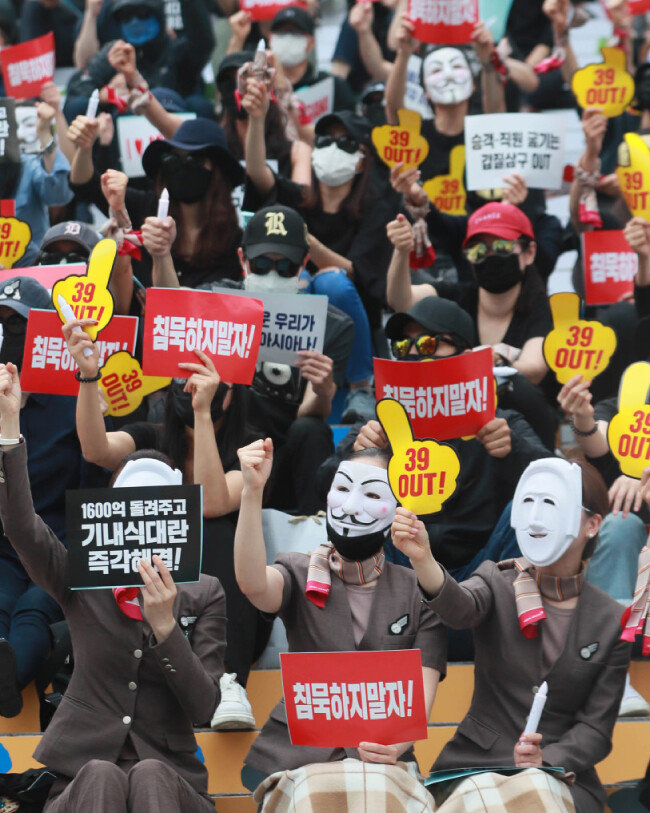 가면과 마스크, 선글라스를 쓴 아시아나항공 직원들이 7월 8일 서울 종로구 세종문화회관 앞 계단에서 열린 ‘노밀(No Meal) 사태 책임 경영진 규탄 문화제’에서 문제 해결을 촉구하는 피켓을 들면서 구호를 외치고 있다. [동아DB]