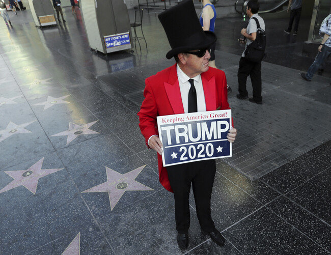 7월 25일(현지 시간) 미국 로스앤젤레스 ‘할리우드 명예의 거리’ 바닥에 설치된 도널드 트럼프 대통령의 별 모양 기념판이 완전히 파손된 가운데, 그 현장에 한 트럼프 대통령 지지자가 ‘미국을 계속 위대하게—트럼프 2020’이라는 글귀가 적힌 피켓을 들고 서 있다. [AP=뉴시스]