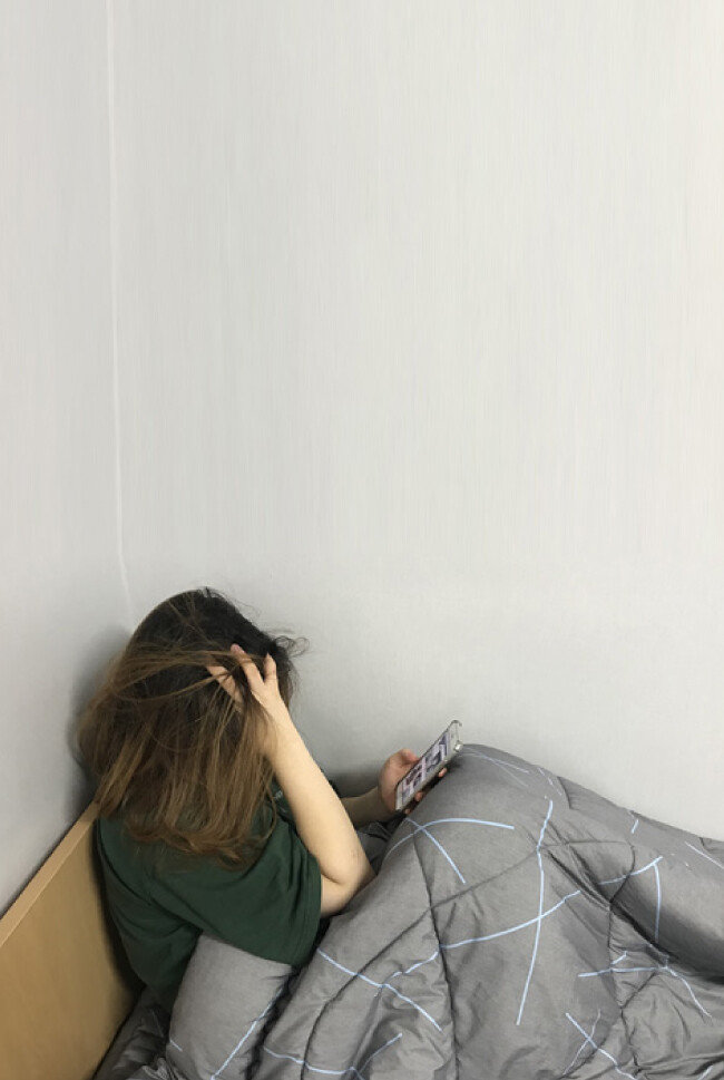 한 여자 대학생이 잠자리에 들기 전 인스타그램을 보면서 우울감을 느끼는 모습.
