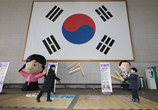 독립의 상징인 대형 태극기 앞에서 두 어린이가 윷놀이를 하고 있다.