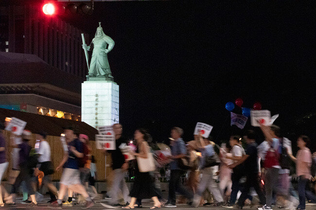 월 3일 아베 신조 일본 총리를 규탄하는 촛불 집회에 참석한 참가자들이 서울 광화문광장을 가로질러 행진하고 있다. 충무공 이순신이 이 행렬을 내려다보고 있다.