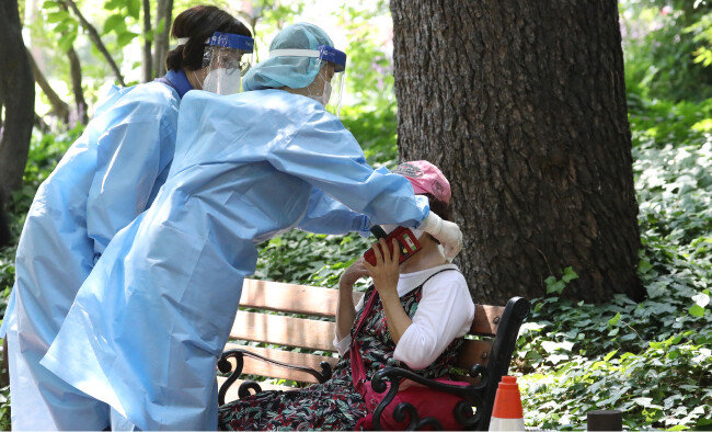 폭염이 계속된 8월 5일 대구시 한 코로나19 임시선별검사소에서 진단검사를 기다리던 60대 여성이 어지러움을 호소하며 주저앉자 근처에 있던 의료진이 달려와 얼음 스카프를 채워주고 있다. [뉴스1]