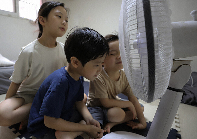 반지하방에서 선풍기 한 대에 의지해 여름을 난 지수(가명)와 두 동생 모습. 세이브더칠드런이 아동 인권 보호를 위해 대역을 사용해 촬영한 것으로, 배경에 등장하는 집은 실제로 지수 남매가 사는 곳이다. [세이브더칠드런 제공]