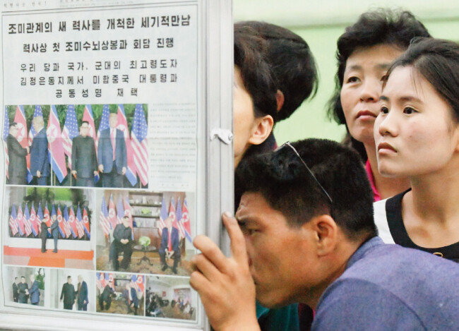 북한 주민들이 6월 13일 평양 지하철역에서 김정은 국무위원장과 도널드 트럼프 미국 대통령의 정상회담 소식을 보도한 ‘노동신문’을 보고 있다. 노동신문은 13일자에서 “조미관계의 새 역사를 개척한 세기적 만남”이라며 12일 정상회담 소식을 4개 면에 걸쳐 보도했다. [평양=AP 뉴시스]
