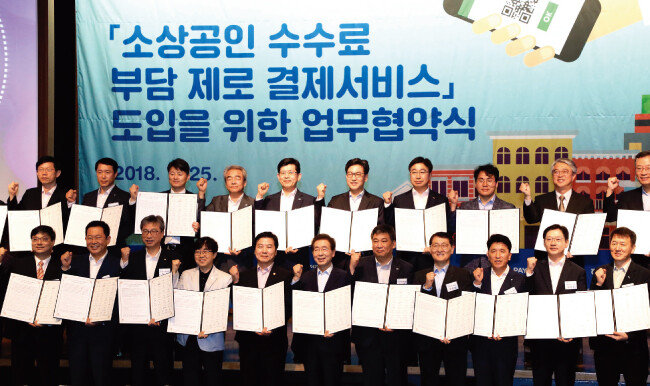 7월 25일 서울 중구 대한상공회의소에서 ‘소상공인 수수료 부담 제로 결제서비스’ 도입을 위한 업무협약식이 열렸다. 이 자리에는 홍종학 중소벤처기업부 장관, 박원순 서울시장을 비롯해 은행계, 산업계, 지방자치단체 등이 참여했다.