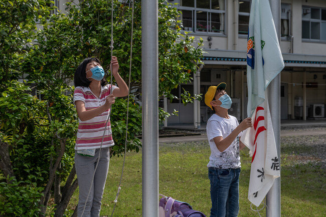 얼굴 마스크를 쓴 아이들이 국기와 교기를 게양한다.