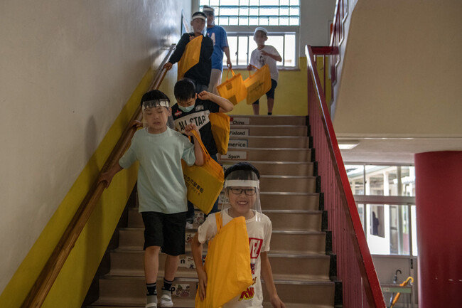 플라스틱 바이저를 착용한 어린이들이 교실로 걸어가고 있다.