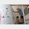 ‘동네드로잉-상상의 정원’이 설치된 옥상에서 밀집모자를 눌러쓴 어린이들이 작품에 색을 입히고 덧 그림을 그려 새로운 동네 모습을 완성하고 있다.＜헬로우뮤지움＞