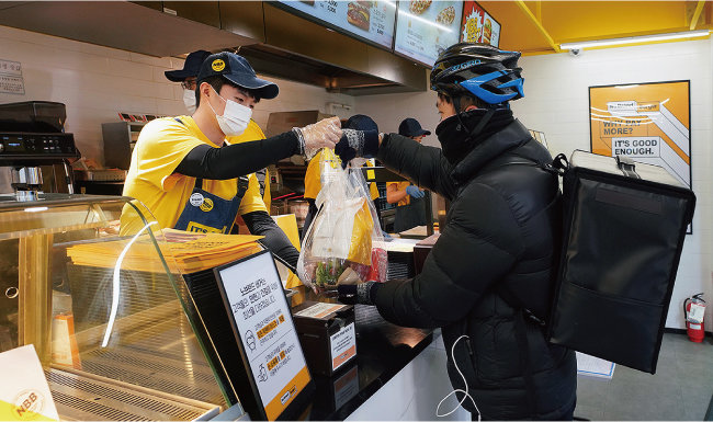 신세계푸드가 운영하는 ‘노브랜드 버거’의 한 매장에서 점원이 배달 라이더에게 햄버거를 전달하고 있다. [신세계푸드 제공]
