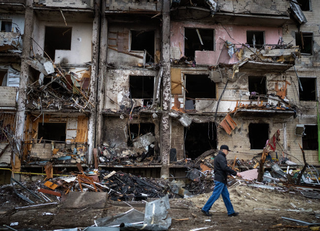 2월 25일 우크라이나 수도 키이우에서 한 시민이 러시아의 로켓 공격으로 파손된 건물 앞을 지나고 있다. [뉴시스]