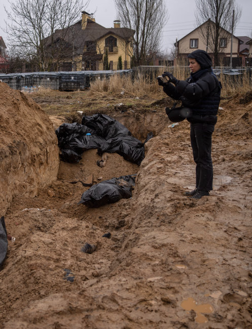 4월 3일(현지 시간) 우크라이나 수도 키이우 인근 소도시 부차의 흙구덩이에 검은 포대에 싸인 시신들이 여기저기 놓여 있다. 러시아군이 부차를 점령했을 동안 우크라이나 민간인을 조직적으로 학살한 후 집단 암매장한 것으로 추정된다. 옆에서 한 기자가 스마트폰으로 현장을 촬영하고 있다. [AP 뉴시스]