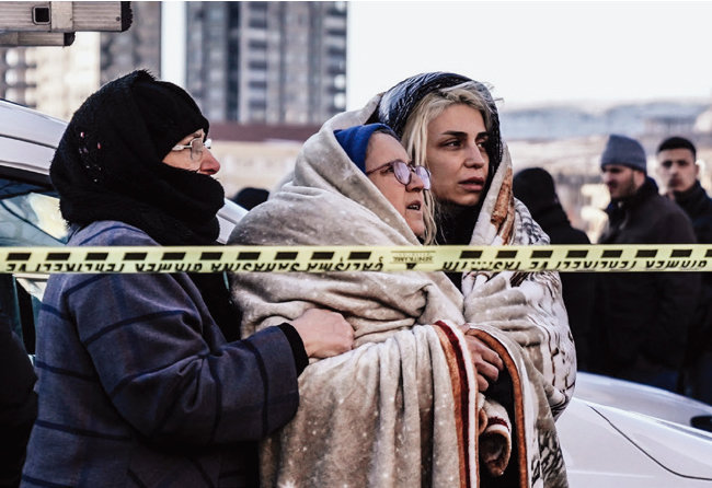2월 7일 세 여성이 튀르키예 가지안테프의 파괴된 건물 잔해 속에서 생존자를 찾는 비상 팀을 지켜보고 있다. [뉴시스]