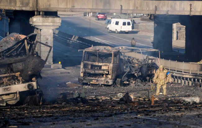 지난해 2월 26일 우크라이나 군인이 키예프의 한 거리에서 폭파된 군용 트럭의 잔해 옆을 지나가고 있다. [AP 뉴시스]