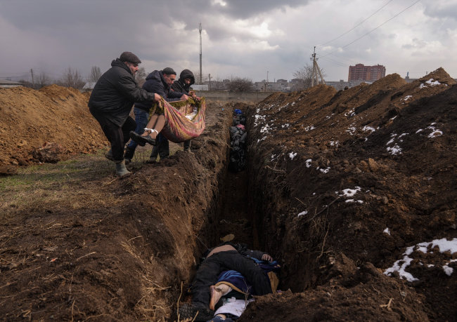 지난해 3월 우크라이나 마리우폴 외곽 지역에서 주민들이 제대로 수습하지도 못한 시신을 고랑에 내려놓고 있다. 카르스텐 브로이어 참모총장은 백승주 회장과 환담하면서 “현장 상황은 끔찍하다”고 말했다. [AP 뉴시스]