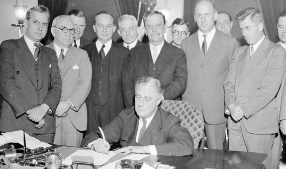 프랭클린 루스벨트 미국 대통령이 1933년 워싱턴DC 백악관에서 뜻을 같이하는 하원의원들에게 둘러싸여 농업 구제 및 통화 인플레이션 관련 법안에 서명하고 있다. Gettyimage