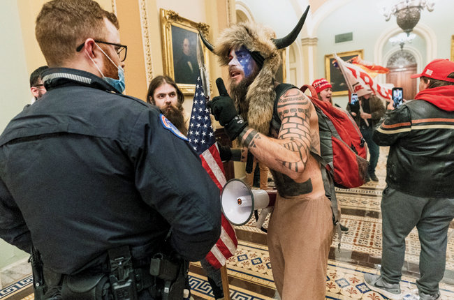 1월 6일(현지시각) 미국 워싱턴 연방의회 의사당에 난입한 ‘큐어넌’ 회원 제이크 앤절리(뿔 달린 모자를 쓴 이)가 경찰관과 대치하고 있다. [AP=뉴시스]
