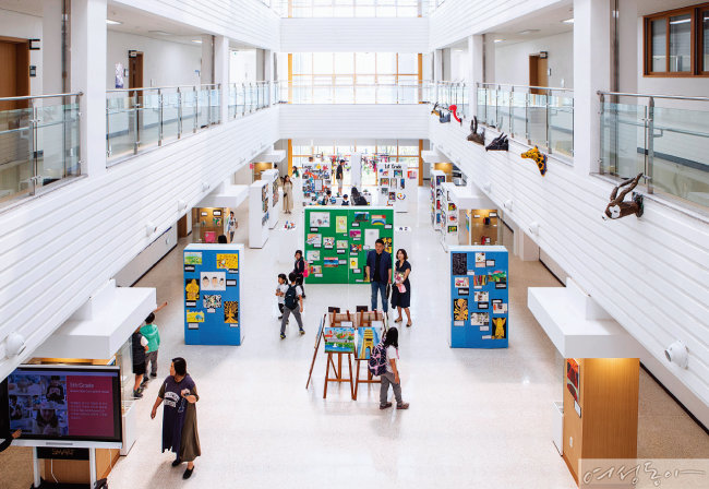 SJA Jeju 행정동 로비에서 학생 및 관람객들이 전시된 미술 작품을 감상하고 있다.
