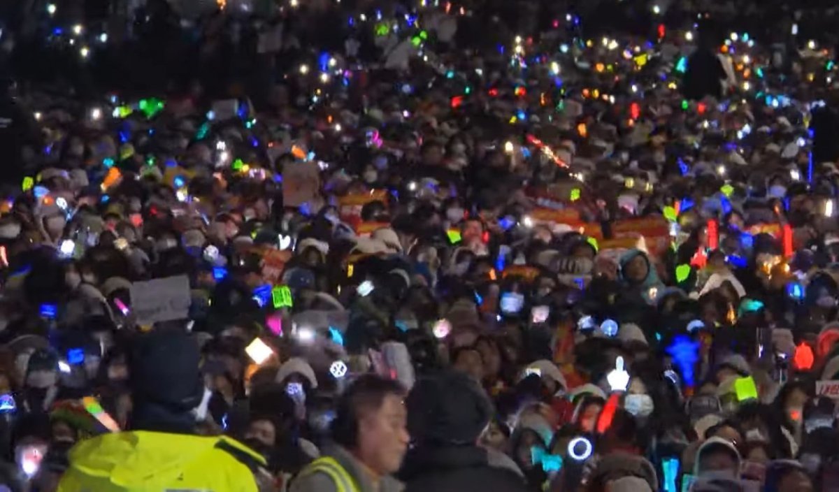 A wave of ‘cheer sticks’, the symbol of K-pop fandom, is spreading throughout the candlelight vigil procession. Photo source|MBC News video capture