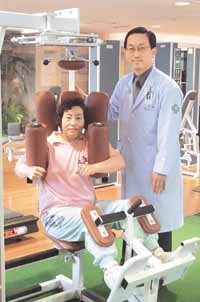 한 중년 여성골퍼가 도은식박사(오른쪽)의 도움을 받으며 '로타리 토르소' 장비로 몸통근육을 단련시키고 있다.