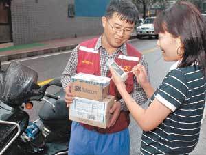 택배로 물건을 배달받은 한 여성이 라이더의 개인휴대단말기(PDA)에 자필서명하고 있다. 이때 배달을 의뢰한 사람의 휴대전화에는 ‘배달 완료’라는 단문메시지(SMS)가 자동으로 발송된다.사진제공 SK텔레콤
