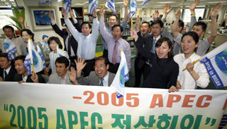 26일 아시아태평양경제협력체(APEC) 정상회의 개최도시가 부산으로 확정되자 부산시 국제협력과 직원들이 APEC 깃발을 흔들며 일제히 환호하고 있다. -부산=연합