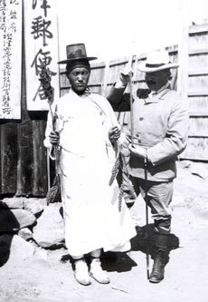 1906년 함북 성진 우편국 앞에서 갓쓰고 도포 입은 조선 젊은이가 들고 있는 곡물의 키를 재고 있는 헤어만 구스타프 테오도르 잔더(오른쪽).-사진제공 국립민속박물관