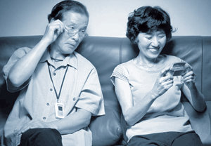 SK텔레콤의 휴대전화 홍보용 책자 ‘현대생활 백서’의 ‘표리부동’편에 실린 사진. 단순한 기능의 ‘효도폰’을 목에 건 남자(왼쪽)가 최신 휴대전화를 사용하는 부인을 물끄러미 쳐다보고 있다. 사진 제공 SK텔레콤