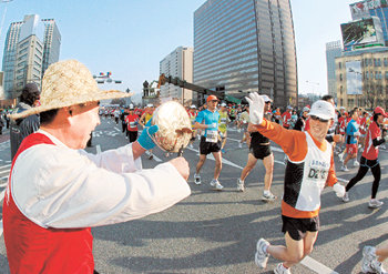 꽹과리 응원 농부 차림을 한 남자의 열성 꽹과리 응원에 서울 세종로 출발선에서 레이스를 시작하는 선수가 답례를 하고 있다.