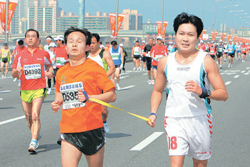 “우리는 한마음” 한 시각장애인(가운데)이 도우미와 서로의 손을 끈으로 묶은 채 35km 지점의 잠실대교를 역주하고 있다.