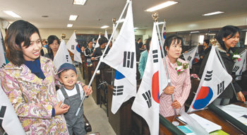 서울 출입국관리사무소에서 열린 귀화증서 수여식에서 결혼이민자들이 태극기를 들고 국민의례를 하고 있는 모습. 동아일보 자료 사진
