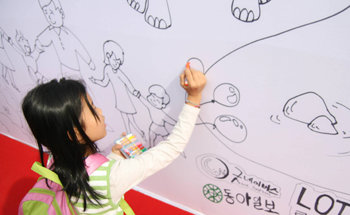 13일 경기 과천시 서울대공원에서 열린 ‘사랑 나눔 그림대회’에 참가한 한 초등학생이 각자 조금씩 그린 부분이 합쳐져 전체를 이루는 ‘월 페인팅’ 벽에 그림을 그려 넣고 있다. 사진 제공 굿네이버스
