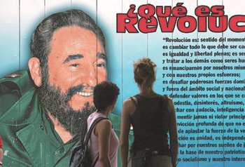 19일(현지 시간) 쿠바의 수도 아바나에서 여성 두 명이 퇴진을 발표한 피델 카스트로 국가평의회 의장의 얼굴이 붙어 있는 벽 게시물을 바라보고 있다. 아바나=로이터 연합뉴스