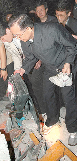 12일 중국 쓰촨 성 두장옌 시를 찾은 원자바오 총리가 붕괴된 학교에서 발견한 신발과 책가방을 집어 들고 있다. 두장옌=AFP 연합뉴스
