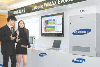 전송 속도 10배 빨라져삼성전자와 한국전자통신연구원이 7일 차세대 통신기술인 모바일 와이맥스 에볼루션을 이용한 인터넷 접속을 세계 최초로 공개 시연했다. 모델들이 노트북 컴퓨터로 인터넷에 연결한 뒤 전송받은 화면을 대형 TV로 보여주고 있다. 연합뉴스