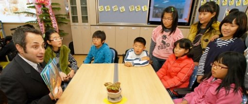 20일 제주 서귀포시 시흥초등학교에서 학생들이 스타벅스의 앨런 제이 힐로위츠 매니저(왼쪽)가 영어로 읽어주는 동화를 흥미로운 표정으로 듣고 있다. 사진 제공 작은도서관만드는사람들