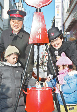 희귀질환인 베체트병을 앓아 한쪽 눈을 실명한 상태에서 자선냄비를 지키고 있는 구세군 사관 한세종 씨(왼쪽 뒤)와 부인 김옥영 씨. 23일 경기 안성시 대천동에서 모금활동을 벌이고 있다. 안성=김재명 기자