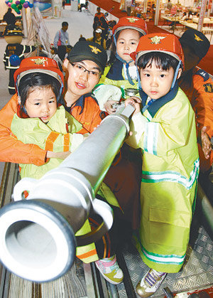 1일 경기 고양시 일산서구 대화동 킨텍스에서 열리고 있는 ‘어린이 교육 체험 박람회’ 행사장을 찾은 어린이들이 한 소방서 직원과 함께 소방차 위에 올라 불을 끄는 체험을 해보고 있다. 고양=이훈구 기자