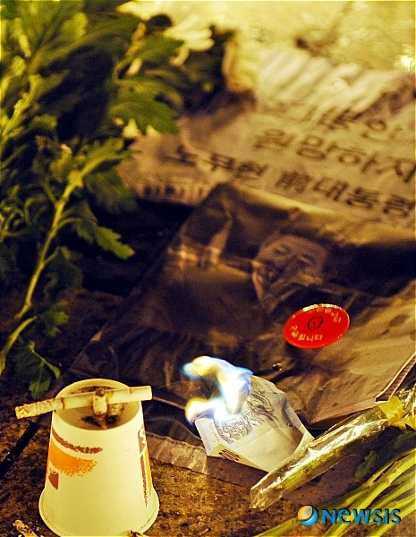 노무현 전 대통령의 서거를 애도하는 각계의 추모 물결이 확산되고 있는 가운데 23일 밤 서울 시청 앞 대한문에서 진행된 ‘故 노무현 전 대통령 추모 분향식’에서 시민들이 노 전 대통령의 서거의 원인이라며 돈을 태우고 생전 즐기던 담배를 사진 앞에 올려놓고 있다.  【서울=뉴시스】