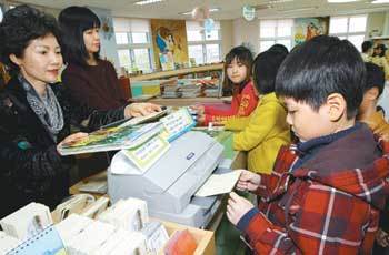 4일 서울 마포구 염리동 한서초교 도서관에서 한 어린이가 ‘독서통장’에 점수를 적립하고 있다. 학생들이 도서관에서 책을 빌리면 이 통장에 점수가 적립되고 높은 점수를 쌓으면 학교에 설치된 만화방을 이용할 수 있다. 한서초교는 3일 교육과학기술부가 발표한 ‘2009학년도 전국학업성취도평가’에서 교과 평균점수 등이 크게 오른 상위 12개교 가운데 하나로 뽑혔다. 왼쪽은 문영혜 교장. 원대연 기자