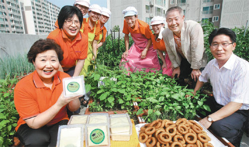 ‘신수동 행복마을주식회사’ 대표 이평심 씨(왼쪽)와 회장 송기창 씨(오른쪽에서 두 번째) 등 주민 주주들이 26일 오후 주민센터 옥상 텃밭에서 두부와 도넛 등 생산품을 내보이며 자신감에 찬 표정을 짓고 있다. 원대연 기자 yeon72@donga.com