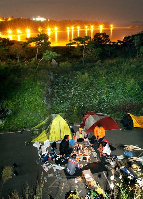 강화도 화도면 장화리의 한 펜션 주차장에 캠프를 마련한 뒤 평화로운 저녁을 맞은 자전거 식객. 소박하게 새우 소금구이에 소줏잔을 기울이다 와인을 갖고 찾아온 이승하 덕분에 예정에 없던 와인파티가 벌어졌다. 캠프 뒤쪽 해안에 설치된 가로등 불빛이 바다에 반사되어 야영 분위기는 황홀했다.