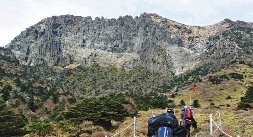 한라산백록담분화구 남벽. 깎아지른 수직벽이 장엄하다. 조각칼로 그은 듯한 거친 칼자국들이 죽죽 위아래로 그어져있다. 빙둘러있는 분화구벽 안쪽이 백록담이다. 한때 용암을 토해냈던 불구덩이가 이젠 물웅덩이가 되어 흰구름을 담는다. 분화구남벽은 겨울엔 눈모자 쓰고, 봄엔 붉은 철쭉으로 목도리를 두른다. 발밑의 늘 푸른 구상나무가 점점이 푸르다. 문득 남벽아래에서 뒤를 돌아보면, 서귀포시내가 가뭇가뭇 발아래 누워있다. 서귀포앞바다 수평선에 뭉게구름이 솜이불처럼 펼쳐있다. 섶섬 문섬 새섬 범섬이 뿅뿅뿅 돋아있다. 제주 한라산=서영수 전문기자 kuki@donga.com