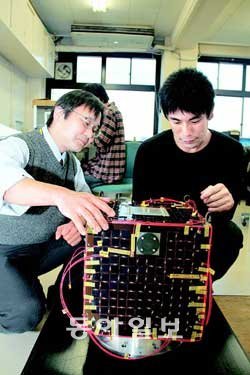 올해 하반기에 우주로 발사될 예정인 프로이테레스 1호의 모습. 다하라 히로카즈 오사카공업대 교수(왼쪽)가 학생과 함께 위성을 살펴보고 있다. 이 대학 학생 50여명이 직접 자재를 구입해 제작했다.