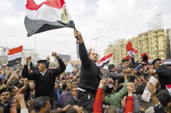 13일 이집트 카이로의 타흐리르 광장에서 검은 제복을 입은 경찰이 동료의 어깨 위에 목말을 탄 채 이집트 국기를 흔들고 있다. 시위 초반에 시위대를 유혈 진압했던 경찰들은 이날 “우리도 시민 편”이라고 주장했다. 카이로=AFP 연합뉴스