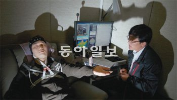 억눌려 감춰졌던 기억도 법 최면이 손을 내밀면 조금씩 고개를 든다. 머리에 뇌파 측정기를 쓴 신진우 기자(왼쪽)가 국립과학수사연구원에서 ‘최면 반응성 검사’를 받고 있다. 함근수 범죄분석실장의 지시에 따라 손에 무거운 사전을 들었다고 상상하는 ‘손 떠오르기’ 최면에 들어간 모습. 양회성 기자 yohan@donga.com