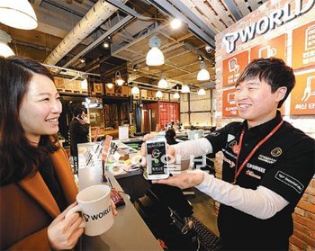 커피전문점 ‘홈스테드’와 SK텔레콤의 휴대전화 대리점이 결합된 경기 부천시 ‘T월드 카페’ 2호점을 찾은 고객(왼쪽)이 12일 커피를 마시며 스마트폰에 대한 설명을 듣고 있다. SK텔레콤은 ‘T월드 카페’를 올해 안으로 전국 15곳으로 확대할 계획이다. SK텔레콤 제공