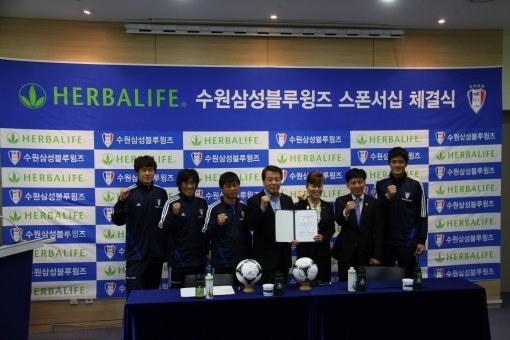 수원 삼성이 15일 화성 클럽하우스에서 허벌라이프와 트레이닝복 스폰서십 체결을 마친 뒤 오근영 수원 단장(가운데)과 정영희 허벌라이프 대표(오른쪽에서 세 번째) 등이 참석한 가운데 포즈를 취하고 있다.  사진제공｜수원 삼성축구단